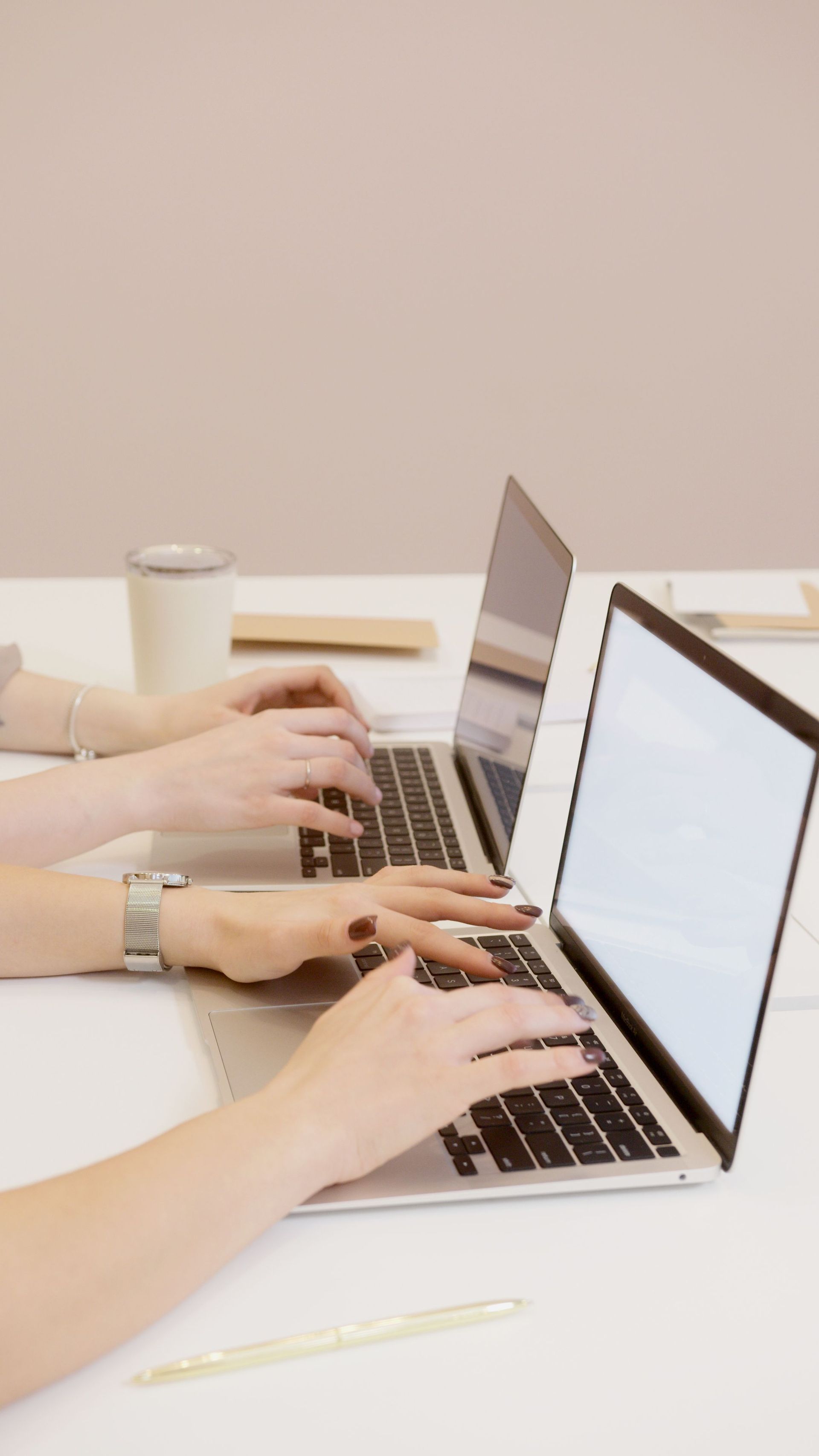 Hands typing on laptops at a white desk in a bright office setting