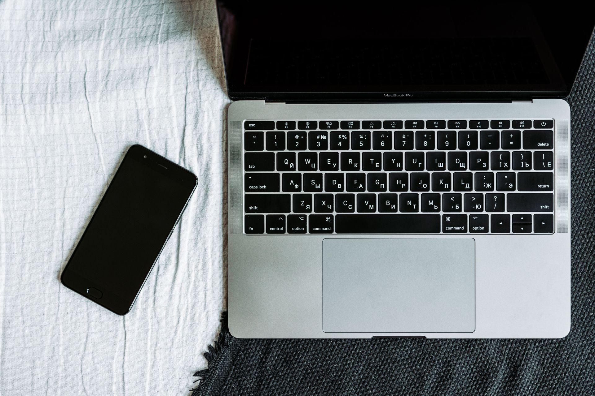 Laptop and smartphone on a bed with a white blanket