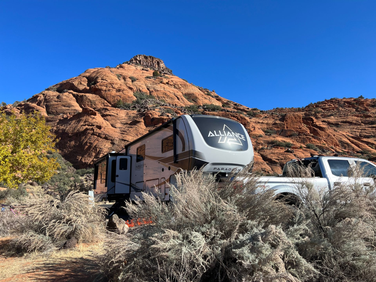 Our home on the road Fifth wheel RV and truck parked beneath red rock desert cliffs, home base for Designs On The Go