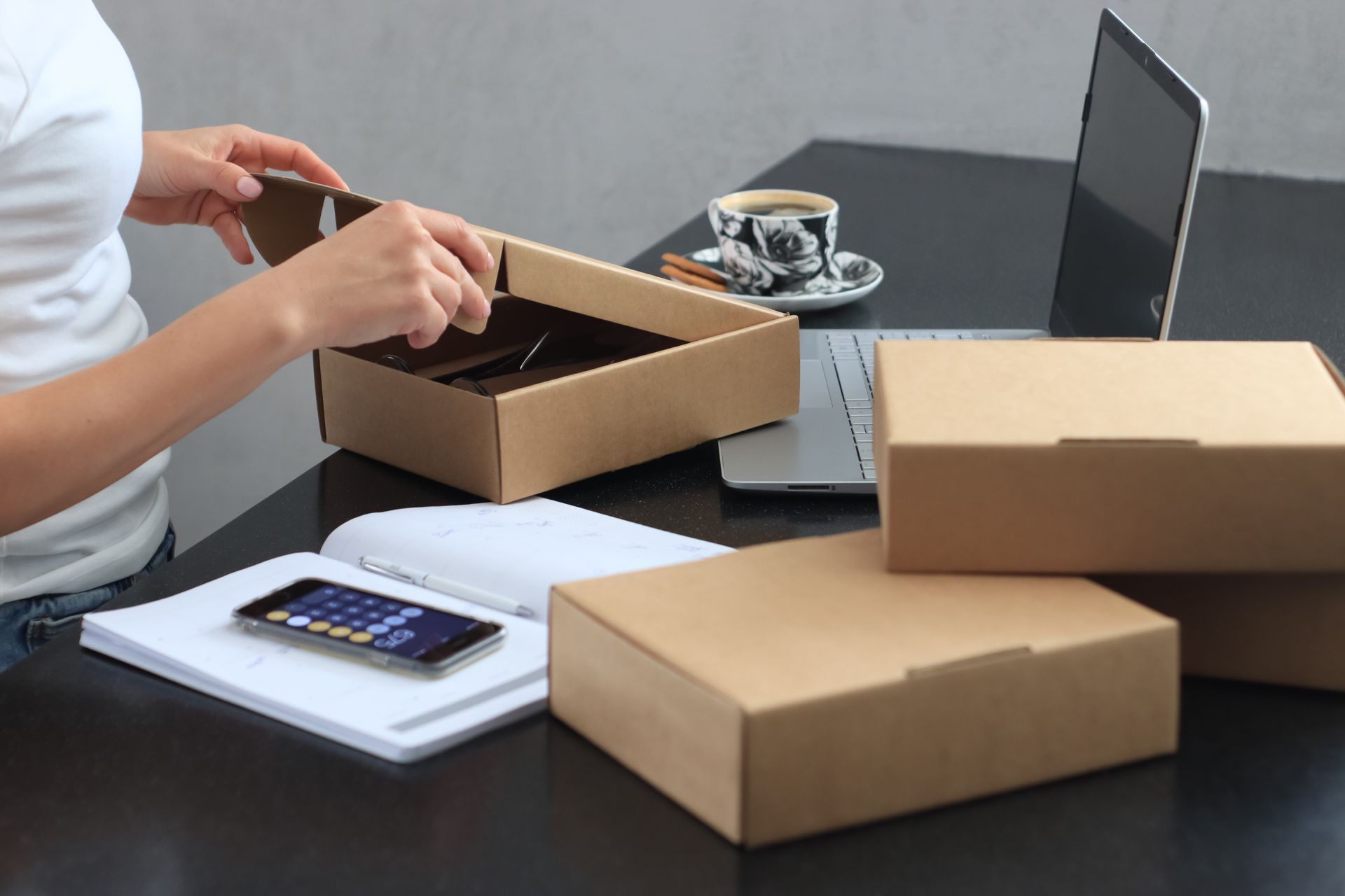 Woman packing orders at her desk with a laptop and shipping boxes representing an active online store