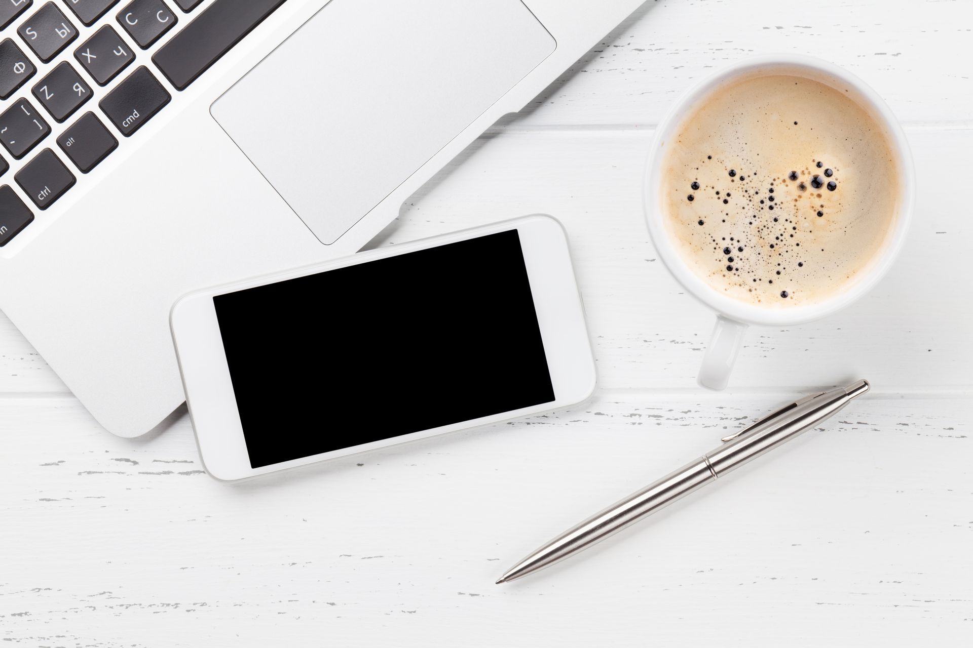 Flat lay of a laptop, smartphone, pen, and coffee cup on a clean white workspace representing online business management