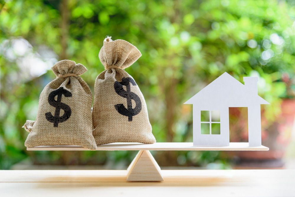A House and Money Bags Are on A Seesaw — A M Conveyancing Pty Ltd In Gold Coast, QLD