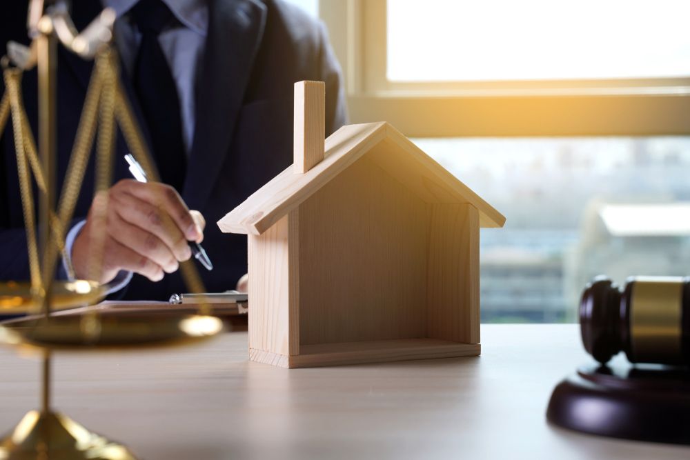 A Man Is Sitting at A Table with A Wooden House and Scales of Justice — A M Conveyancing Pty Ltd In Gold Coast, QLD