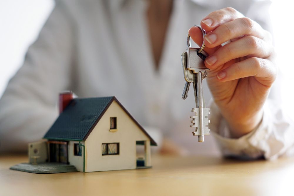 A Woman Is Holding a Pair of Keys in Front of A Model House — A M Conveyancing Pty Ltd In Tweed Heads, NSW