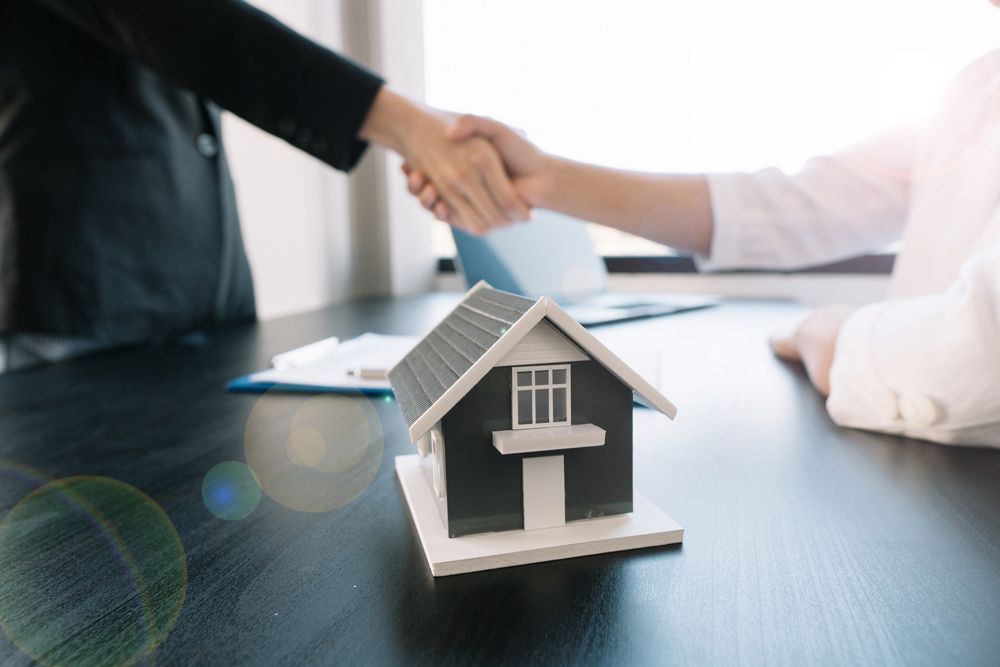 A Woman Is Shaking Hands with A Man in Front of A Model House — A M Conveyancing Pty Ltd In Tweed Heads, NSW