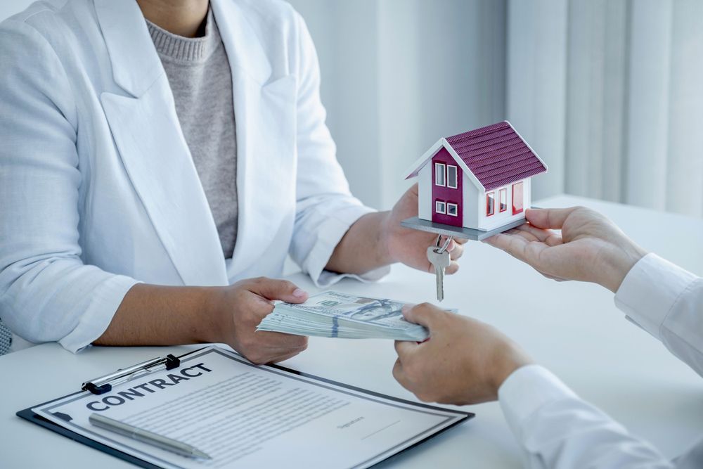 A Woman Is Handing a Model House and Keys to A Man — A M Conveyancing Pty Ltd In Tweed Heads, NSW