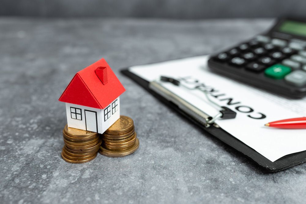 A Small House Is Sitting on Top of A Pile of Coins Next to A Calculator and A Pen — A M Conveyancing Pty Ltd In Tweed Heads, NSW