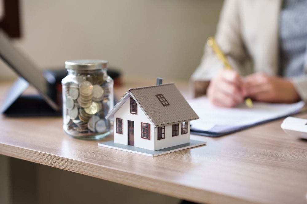 A Model House Is Sitting on A Desk Next to A Jar of Coins — A M Conveyancing Pty Ltd In Tweed Heads, NSW
