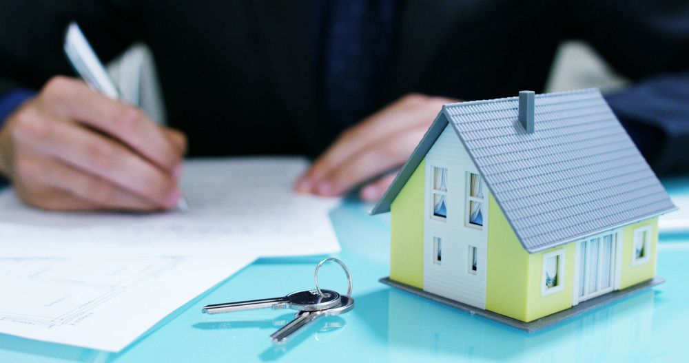A Person Is Writing on A Piece of Paper Next to A Model House and Keys — A M Conveyancing Pty Ltd In Tweed Heads, NSW
