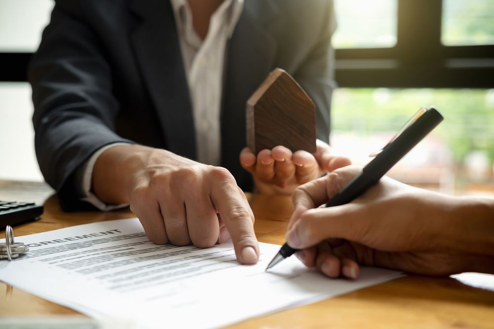 A Man Is Holding a Model House and A Woman Is Signing a Document — A M Conveyancing Pty Ltd In Palm Beach, QLD