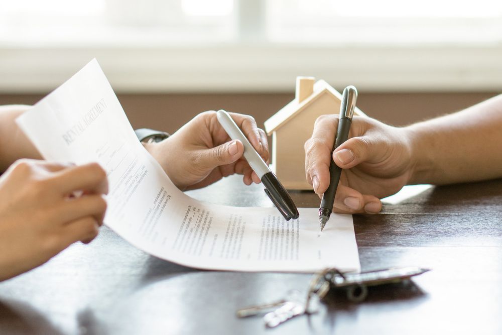 A Couple of People Are Sitting at A Table Signing a Document — A M Conveyancing Pty Ltd In Palm Beach, QLD