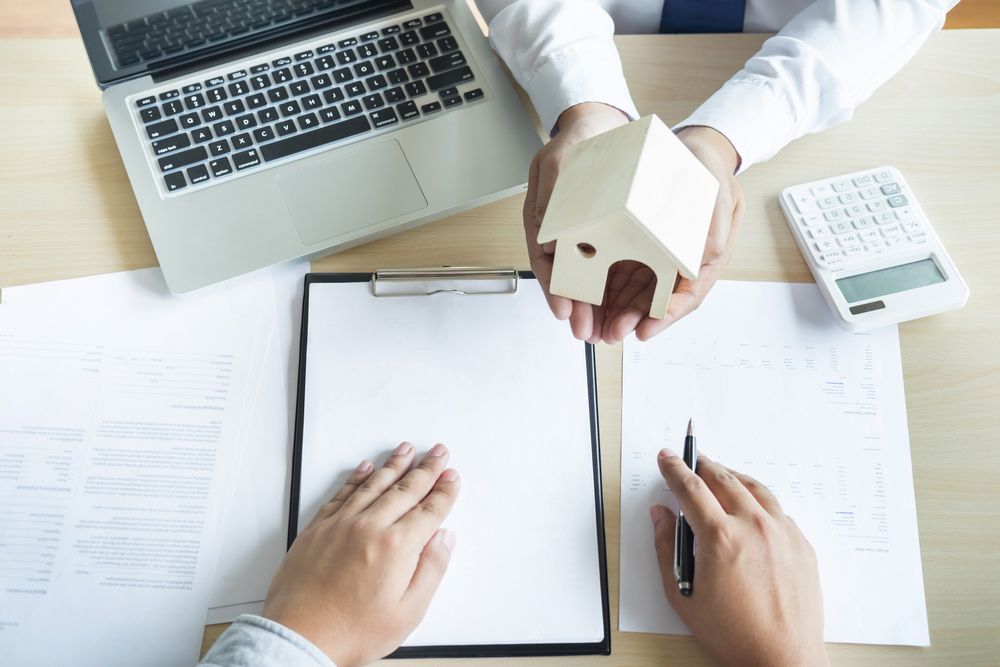 A Man Is Holding a Model House in His Hands While a Woman Is Signing a Document — A M Conveyancing Pty Ltd In Palm Beach, QLD