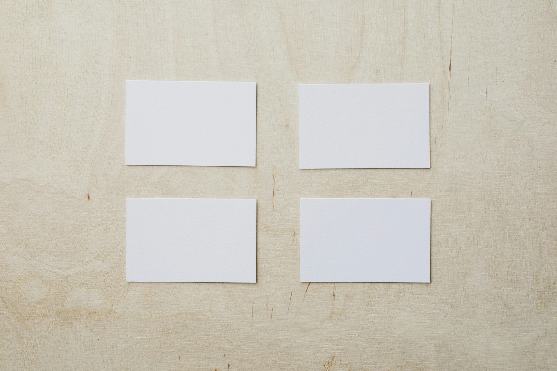 Four blank white business cards on a light wood grain background.