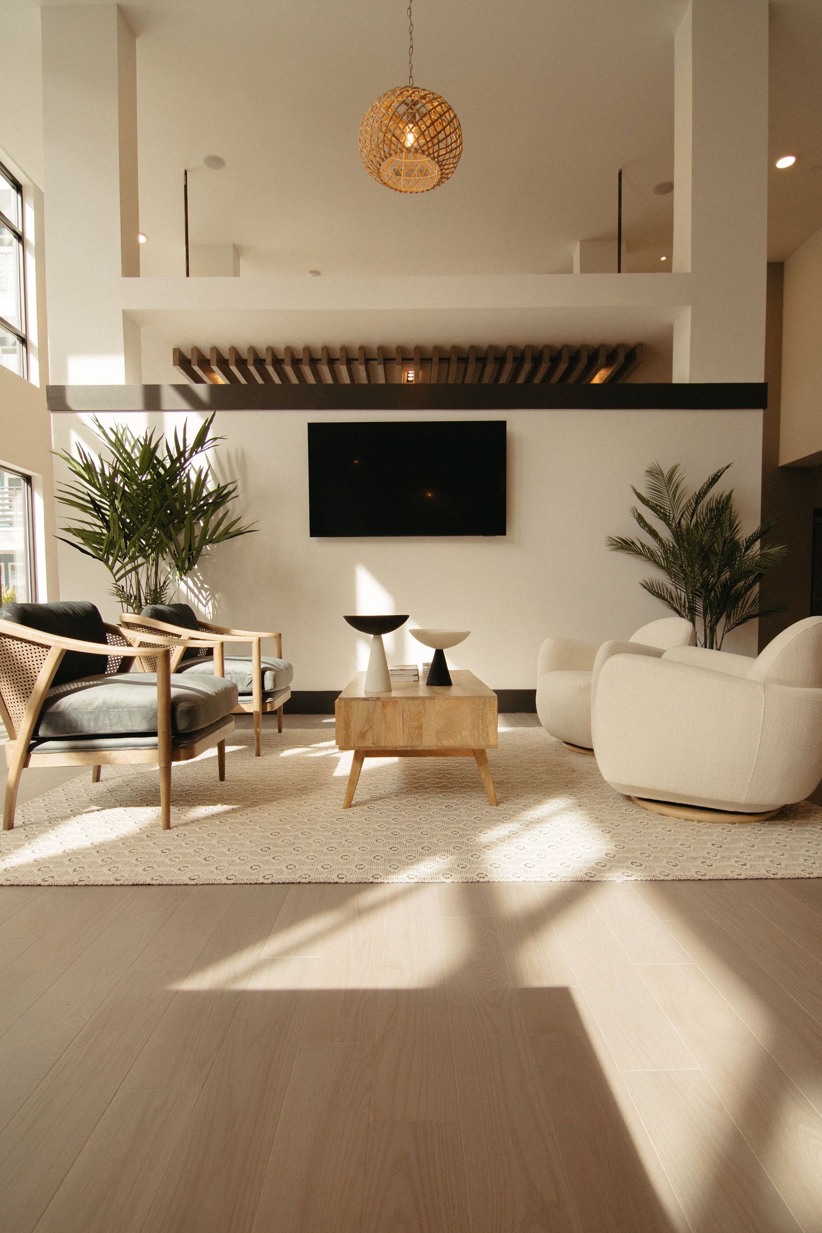 Modern living room with neutral tones, including a wooden coffee table, two armchairs, and a television mounted on the wall.