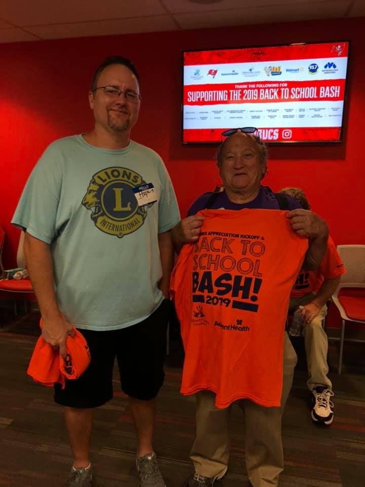 A man and a woman are holding an orange back to school bash shirt
