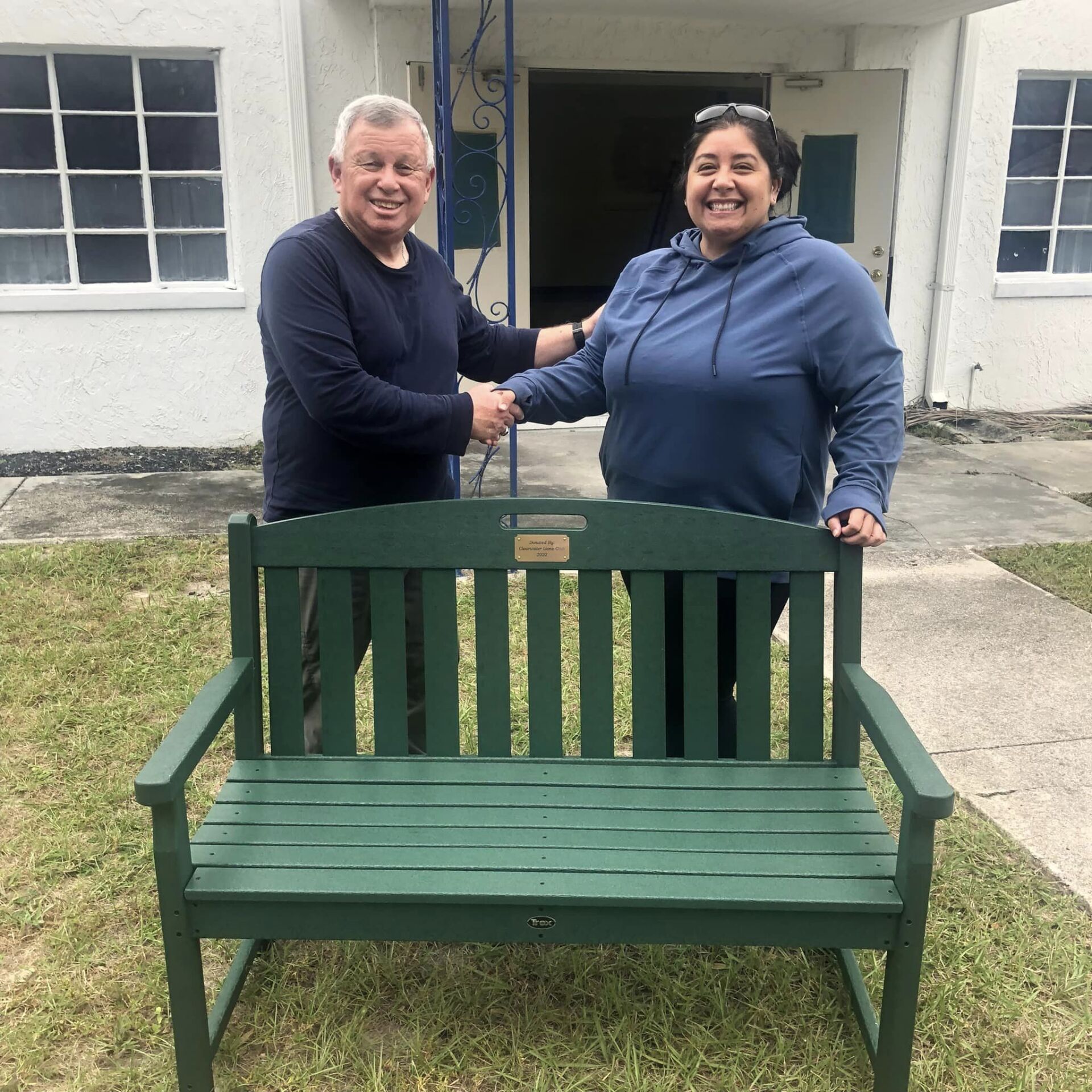A man and woman shaking hands in front of a green bench