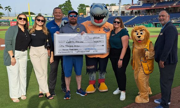 A group of people standing on a baseball field with a mascot holding a check.