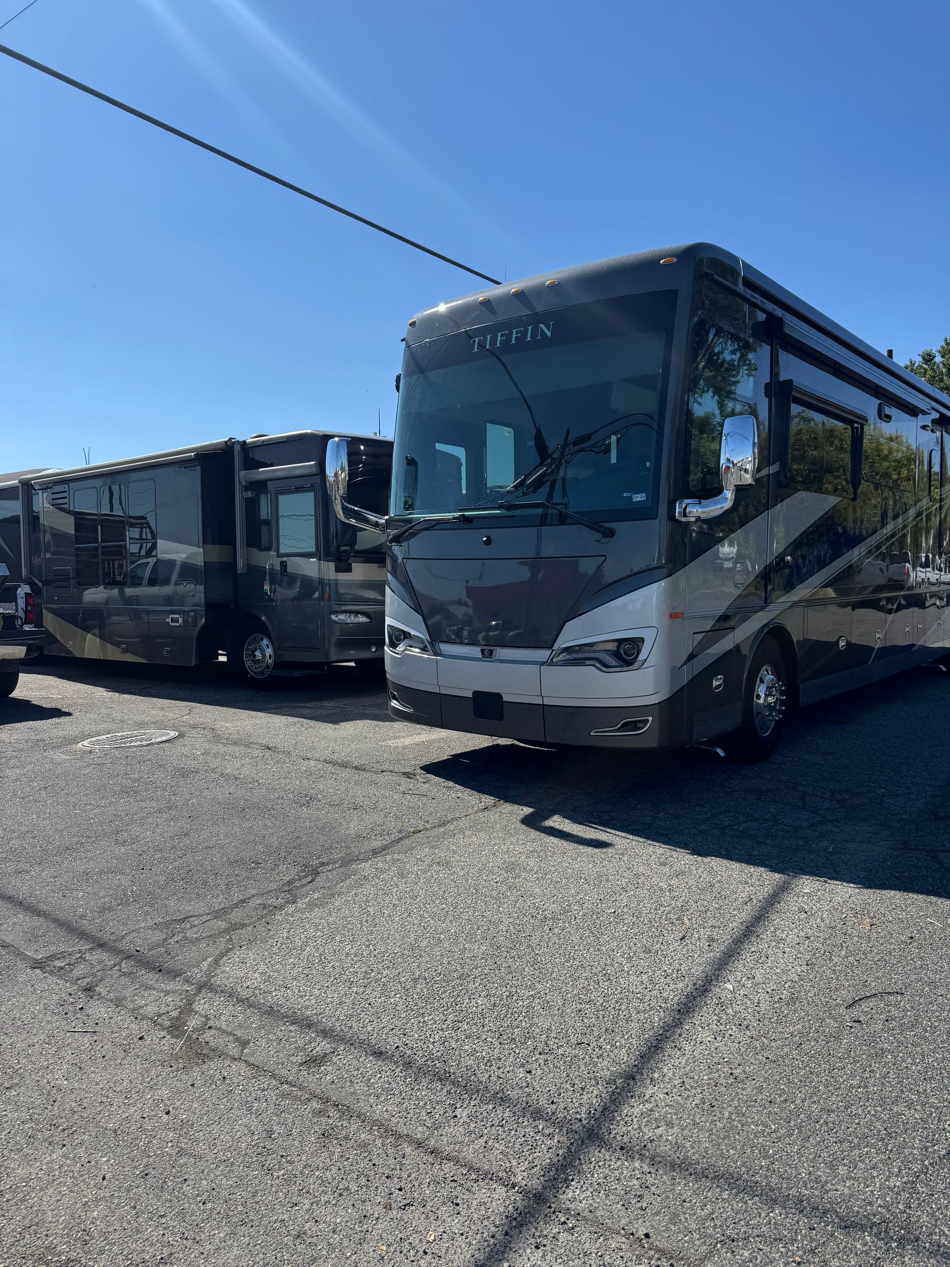 Two large, gray and silver RVs parked on gravel under a blue sky.