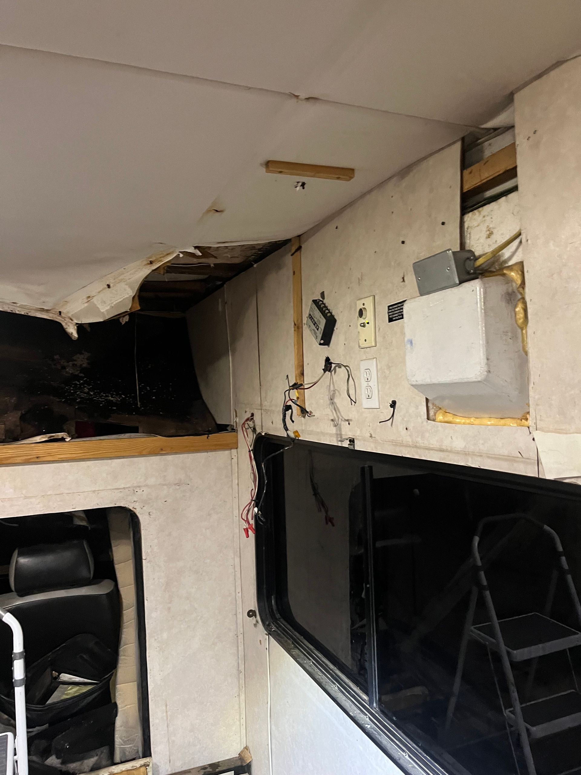 Interior of a damaged RV with exposed ceiling, walls, electrical components, and window.