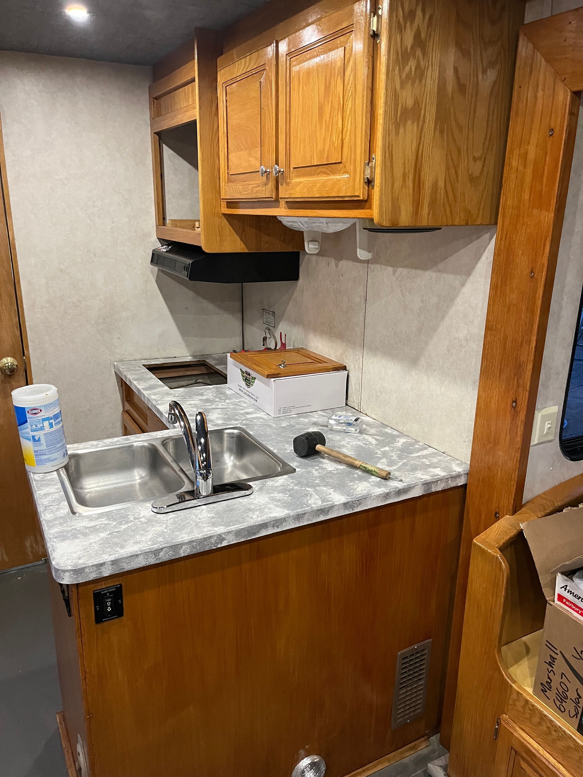 RV kitchen: Sink, stove, cabinets, and microwave. Wooden cabinets, gray countertop, and basic appliances.