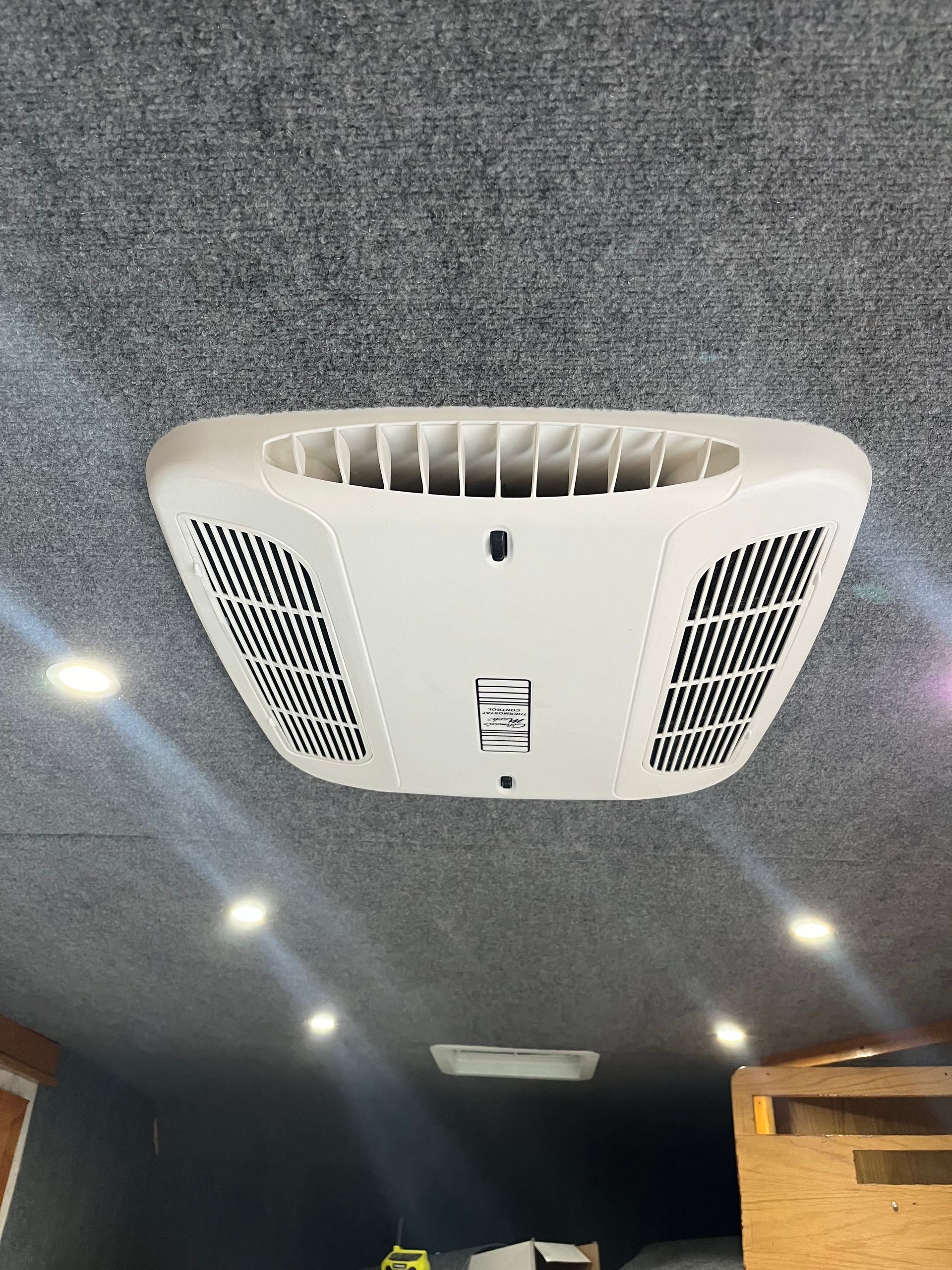White air conditioning unit on a gray textured ceiling, with recessed lights.