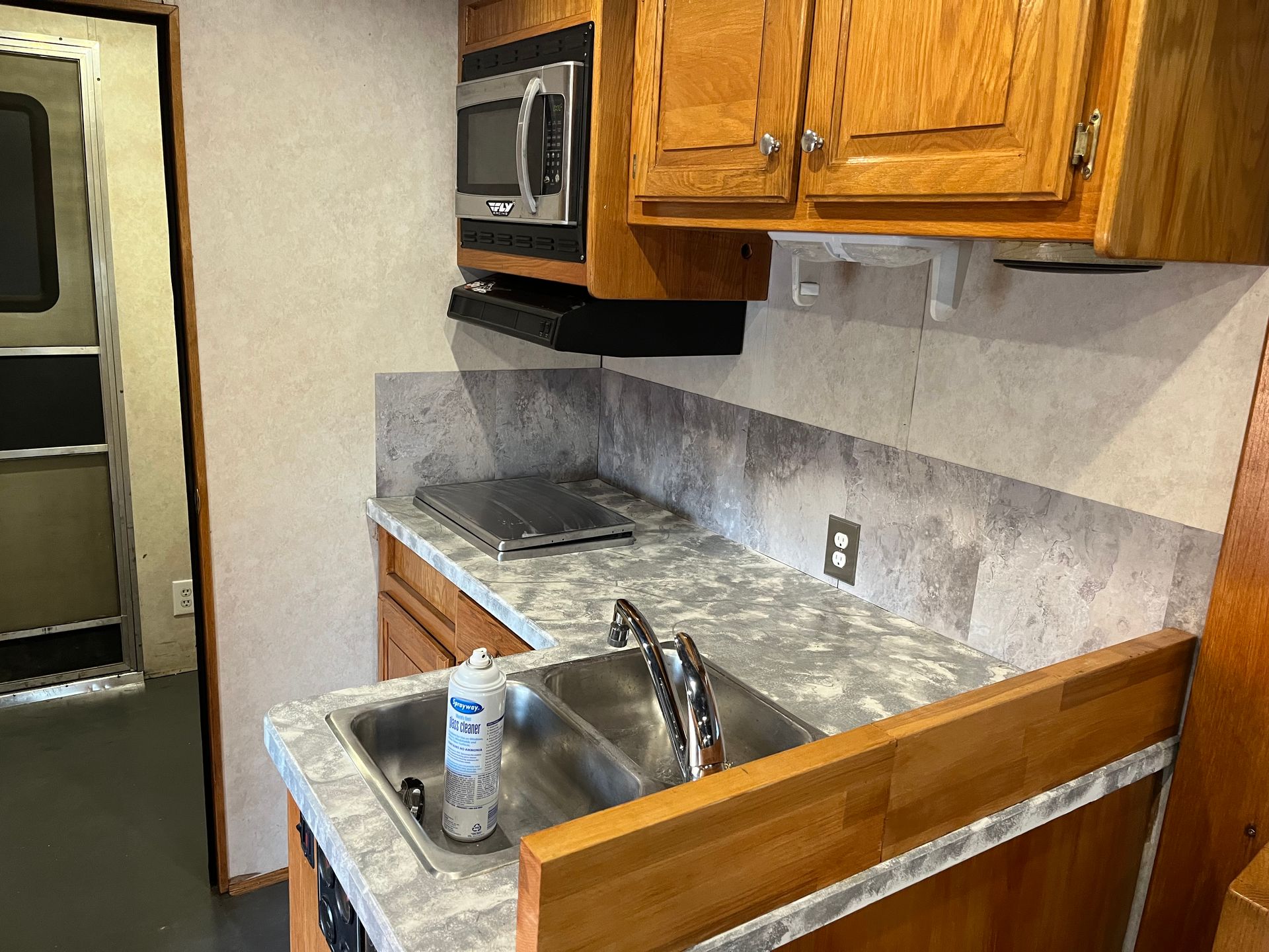 RV kitchen with a sink, stovetop, microwave, and wooden cabinets.