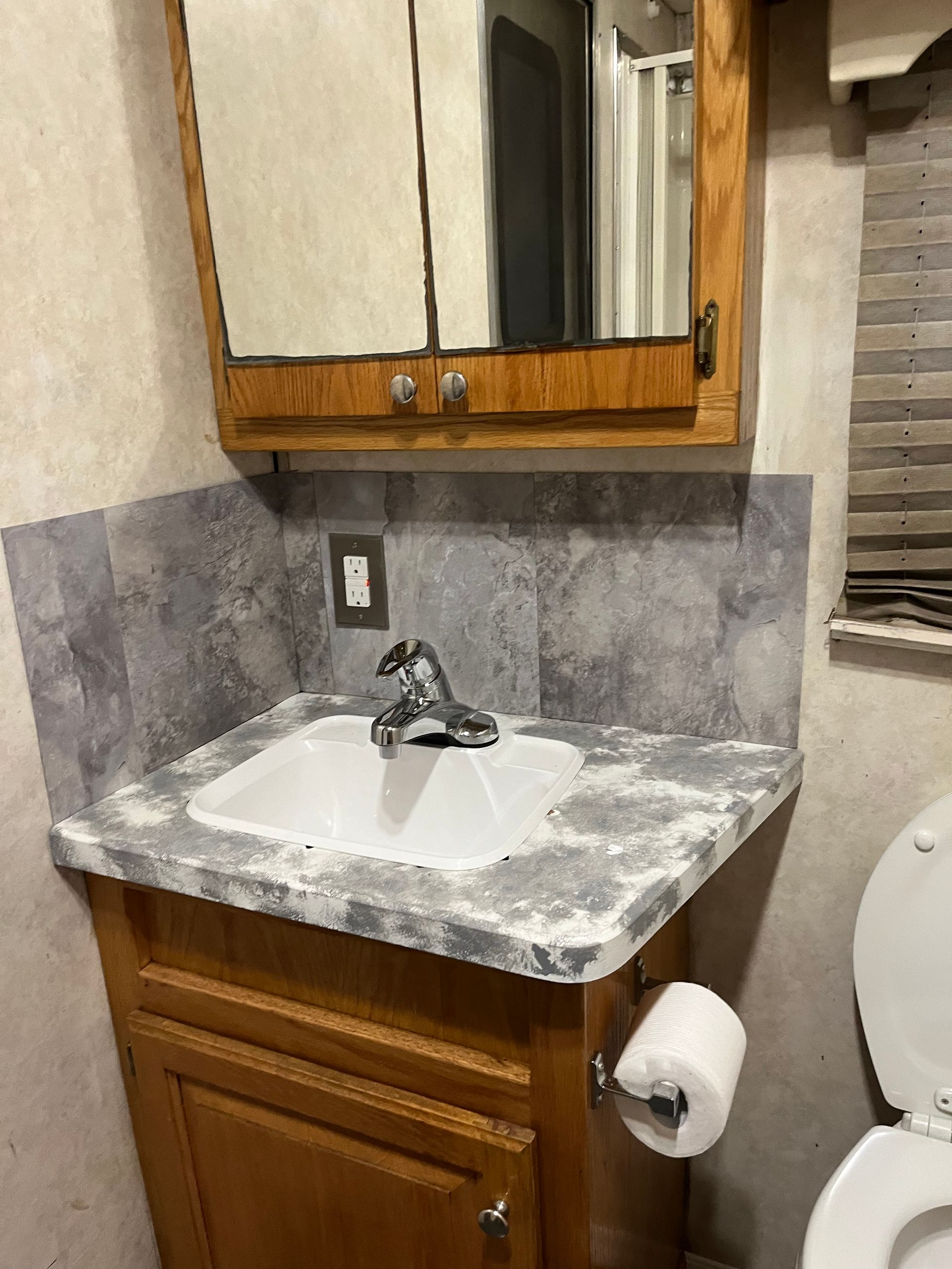 Bathroom interior with vanity, sink, mirror, toilet, and gray tiled backsplash in an RV.