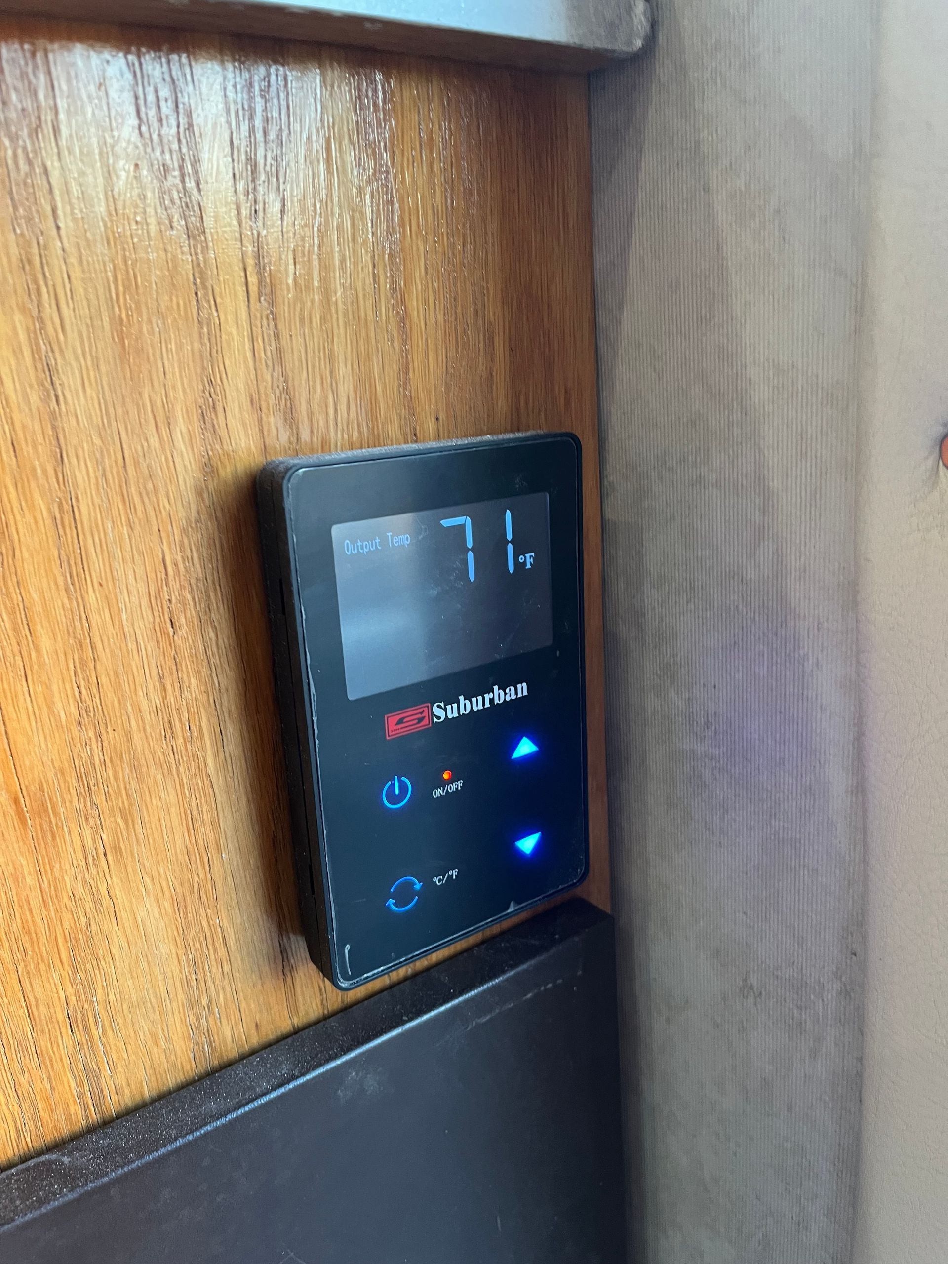 Black thermostat mounted on wood paneling; displays 71 degrees.
