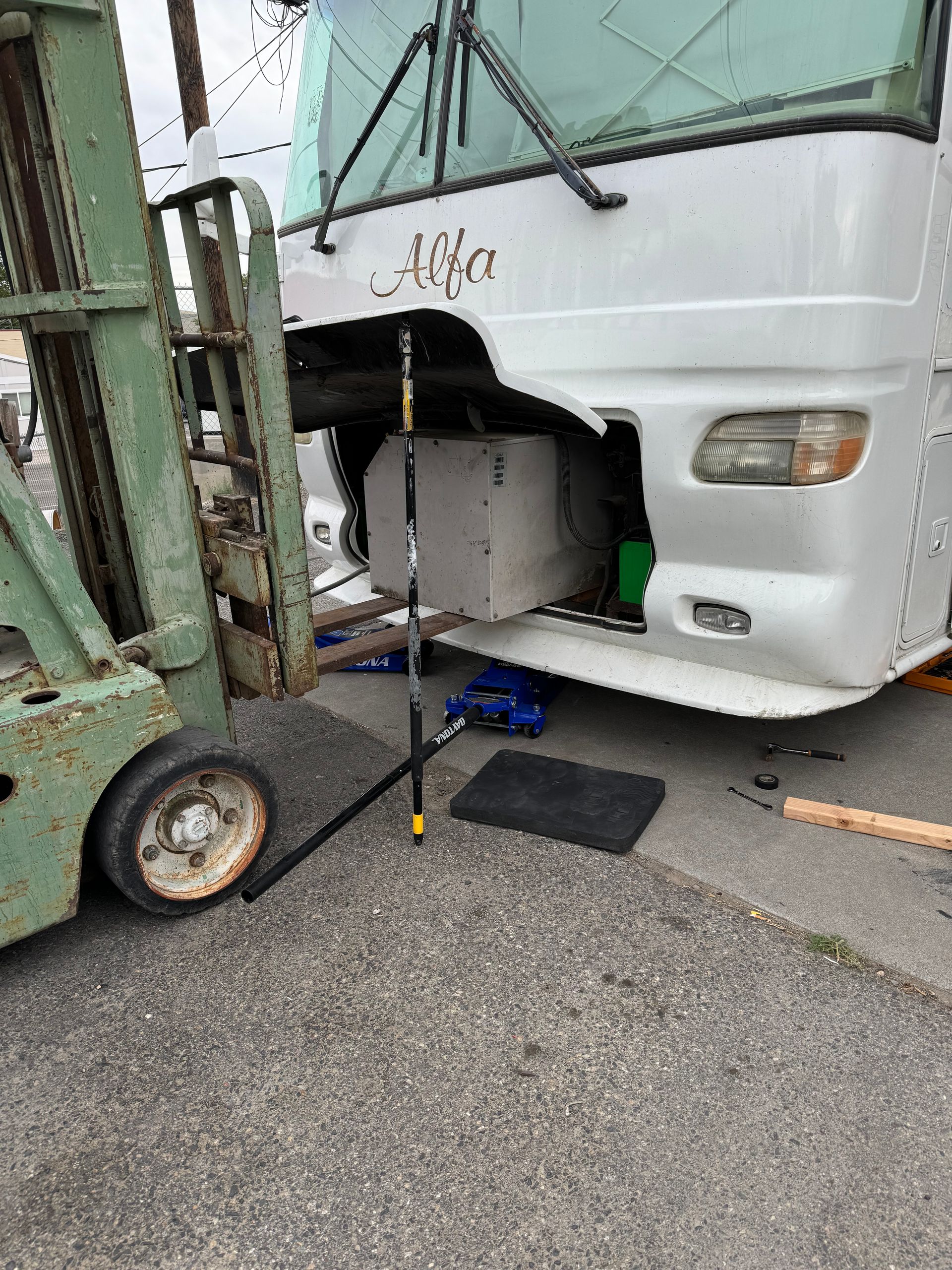 A forklift next to a white motorhome with open front compartment; on a paved surface.