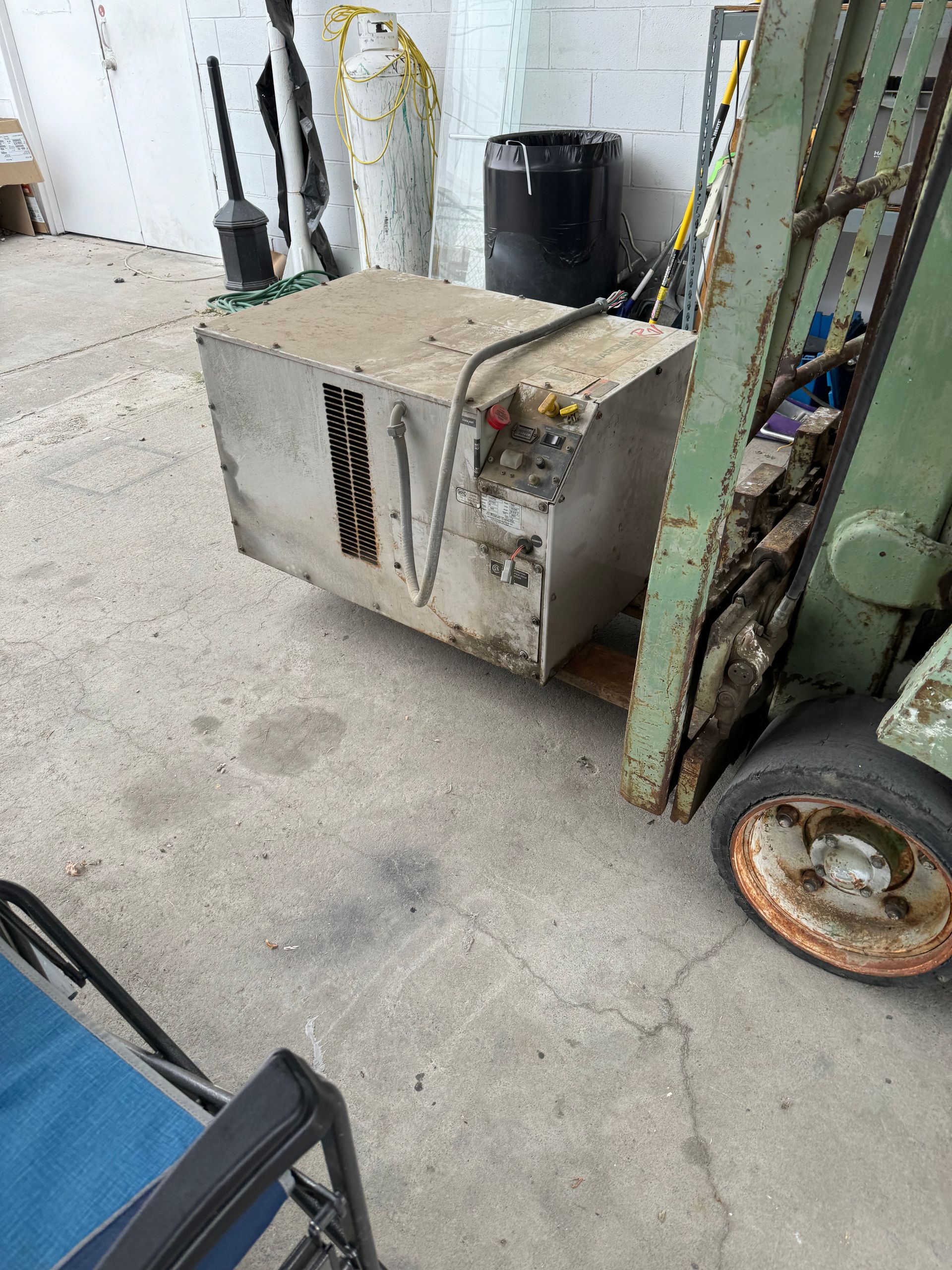 Forklift lifting a large, weathered metal box in a concrete-floored space, possibly a garage or storage area.