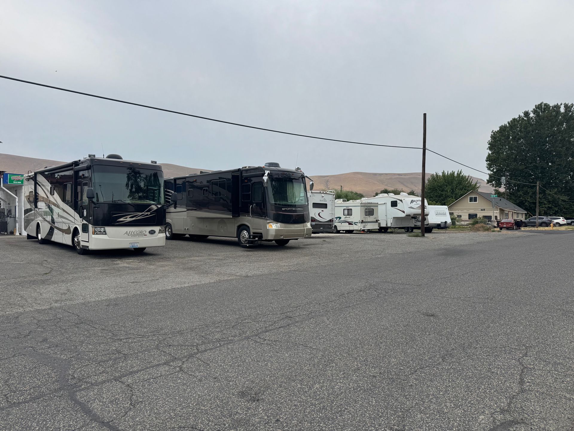 RVs and trailers parked on a gravel lot under a cloudy sky.