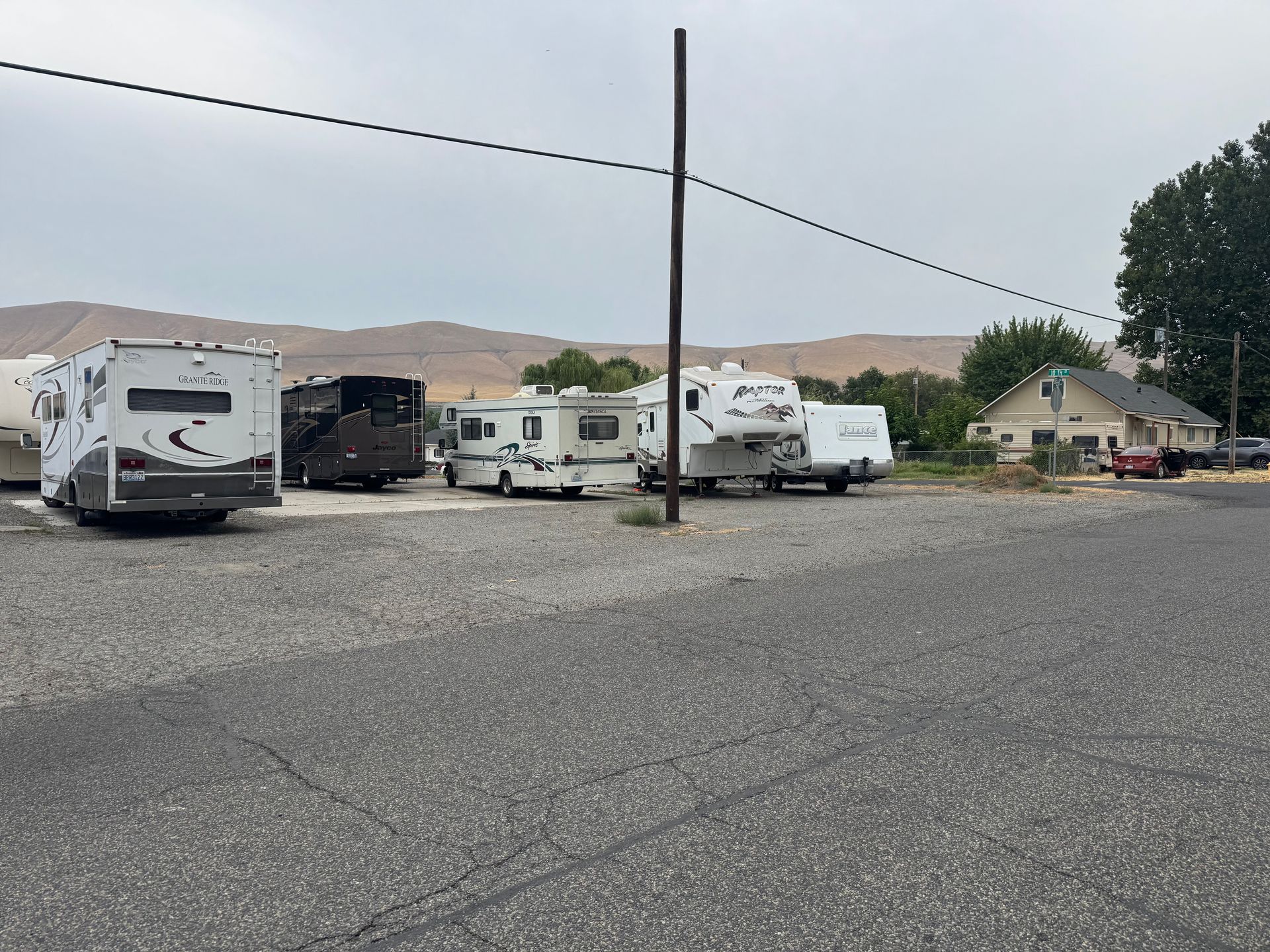 RVs parked on a gravel lot under a cloudy sky, near a building and a mountain range.