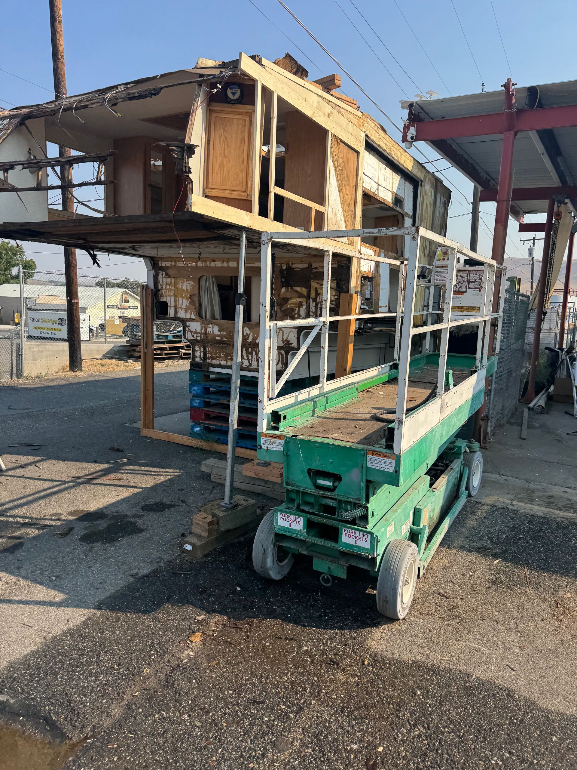 A partially dismantled structure sits on a green lift in an outdoor industrial area.