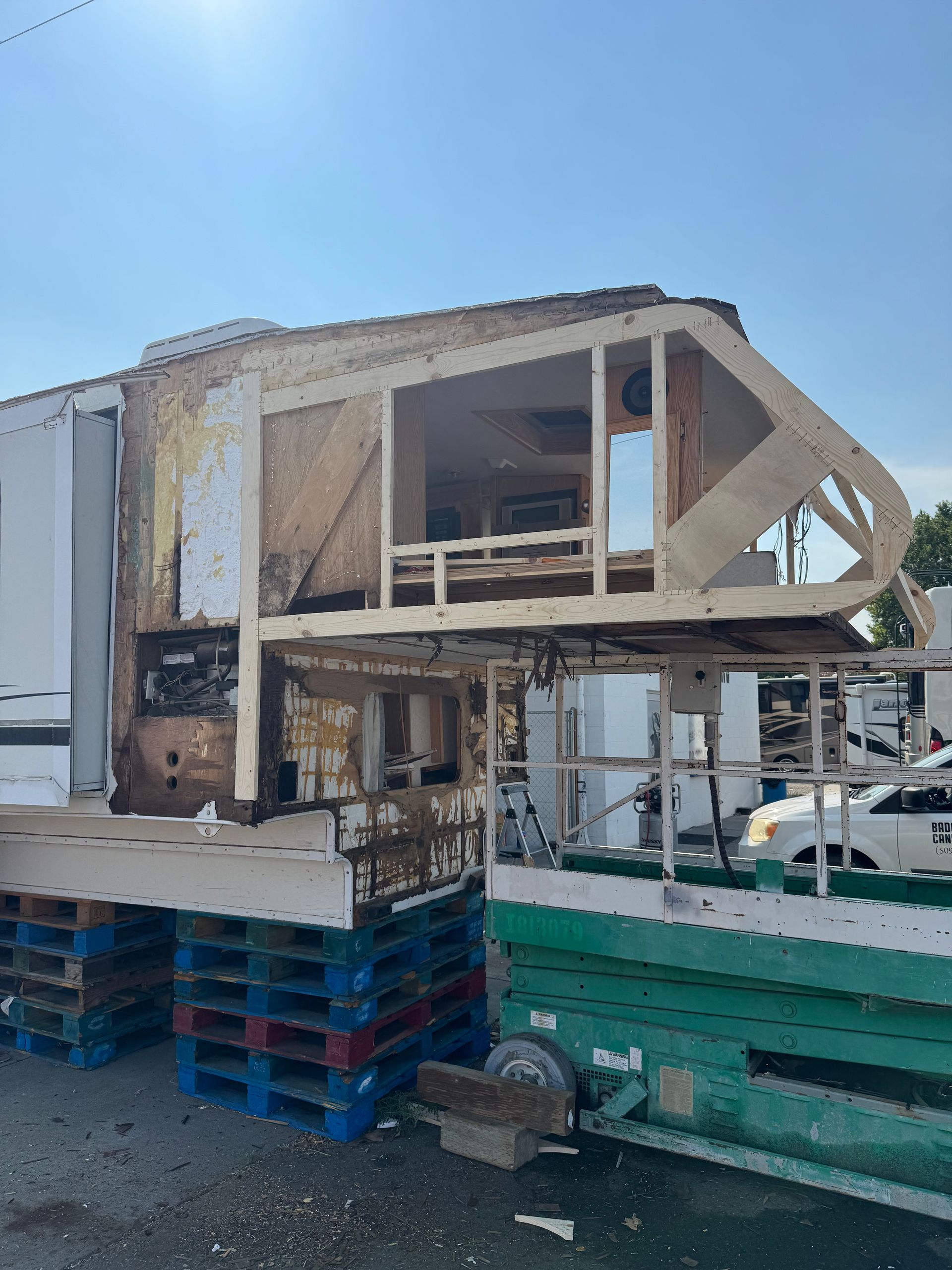 RV camper stripped of exterior siding, supported on pallets. Wooden frame exposed.