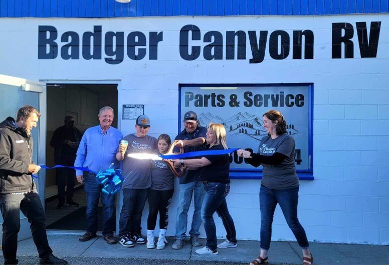 Ribbon-cutting at Badger Canyon RV. People cutting a blue ribbon in front of a building with blue and white accents.