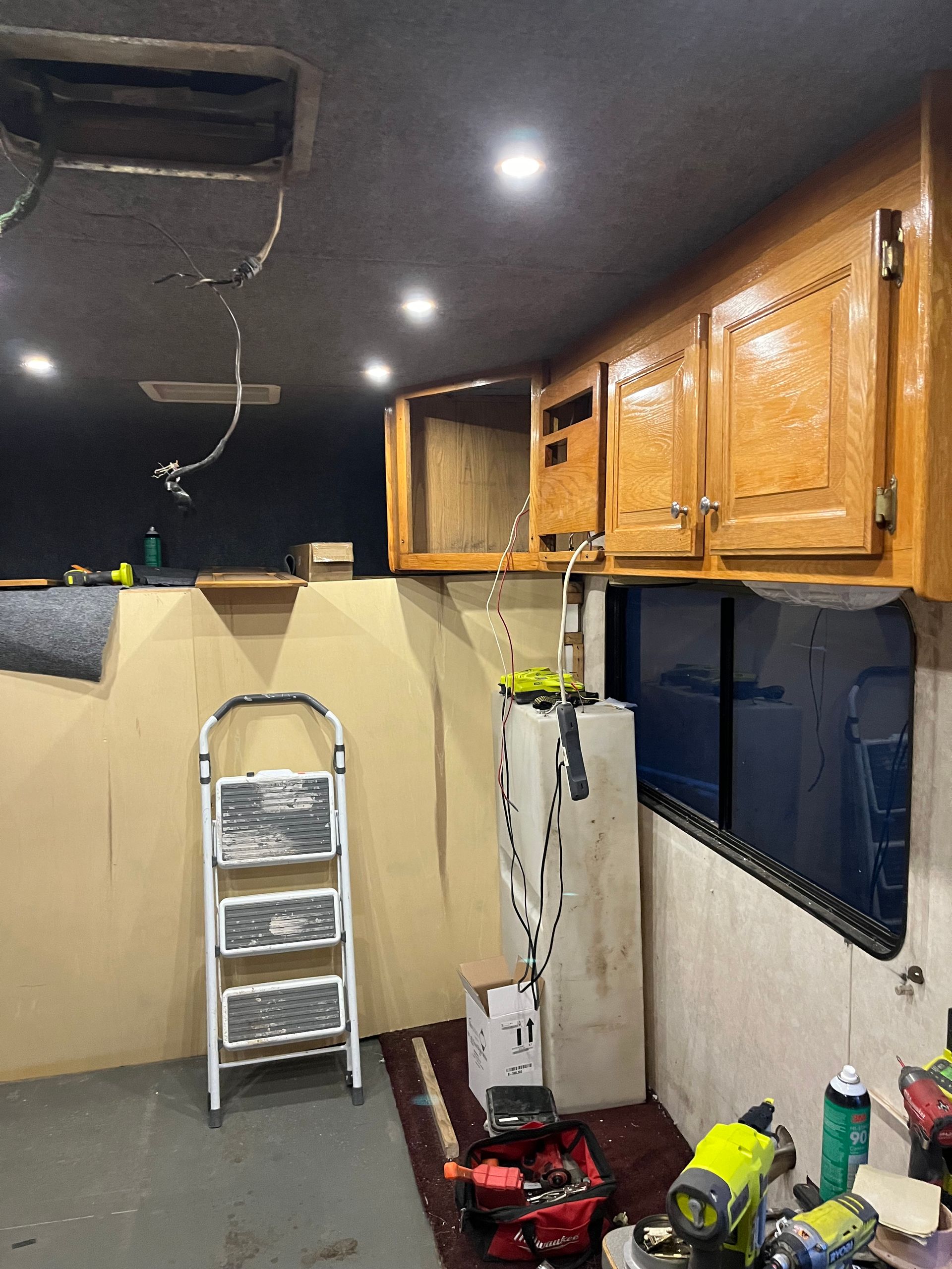 Interior view of a camper being renovated. Cabinets, wiring, a ladder, and tools are visible.