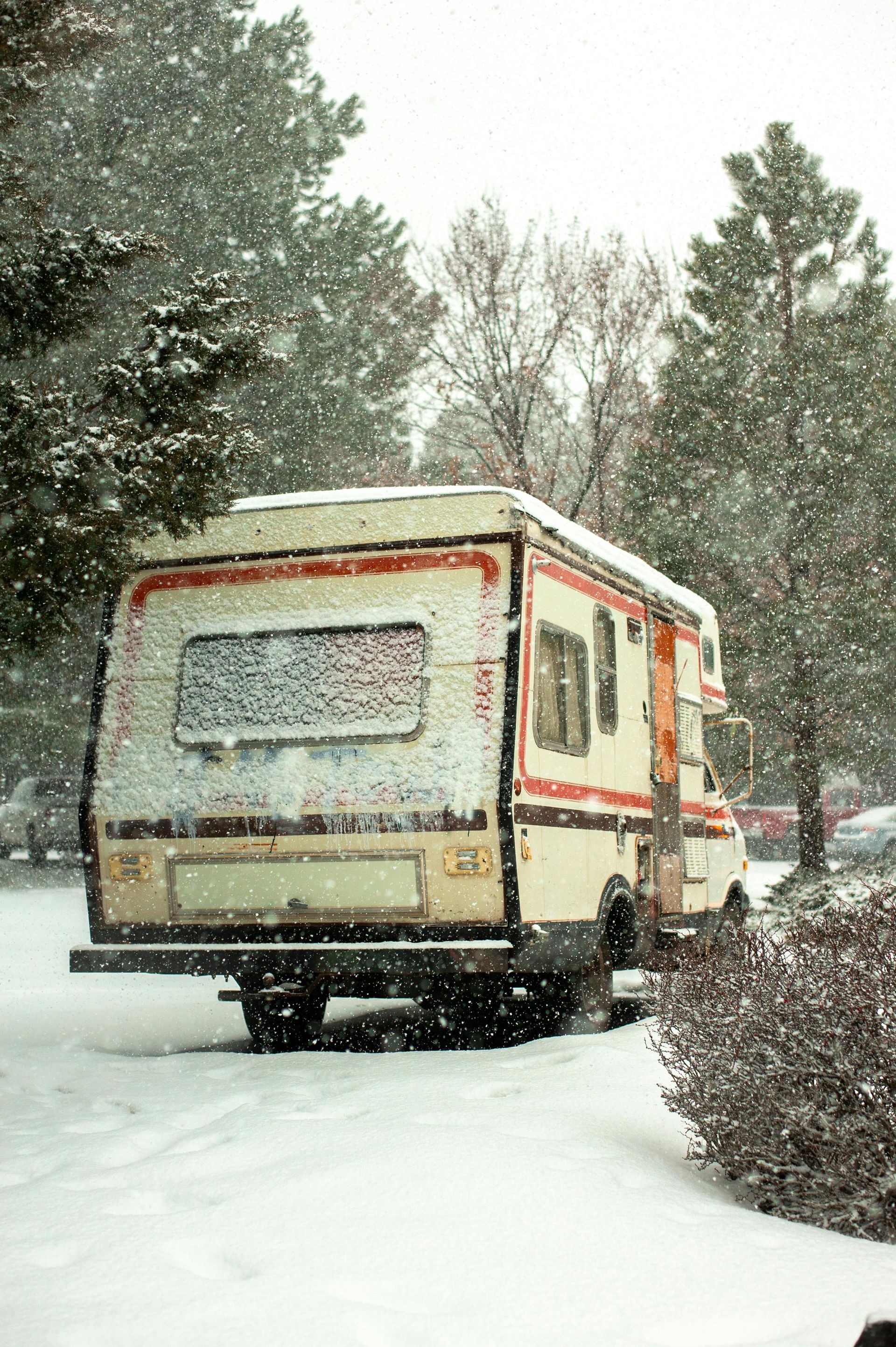 White postal truck parked in snow, with red and black stripes, in a snowy wooded area.