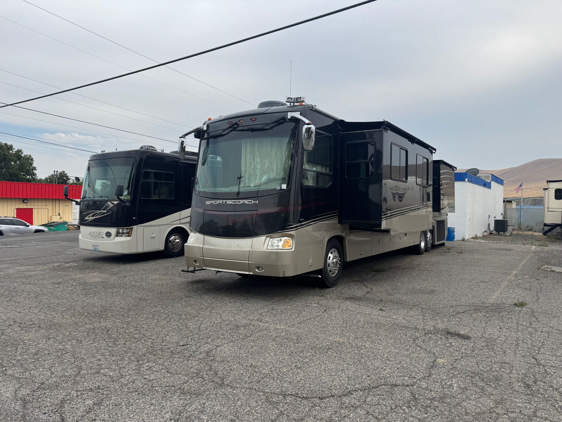 Two large RVs parked on gravel. One is black and tan, the other is black. Overcast sky.