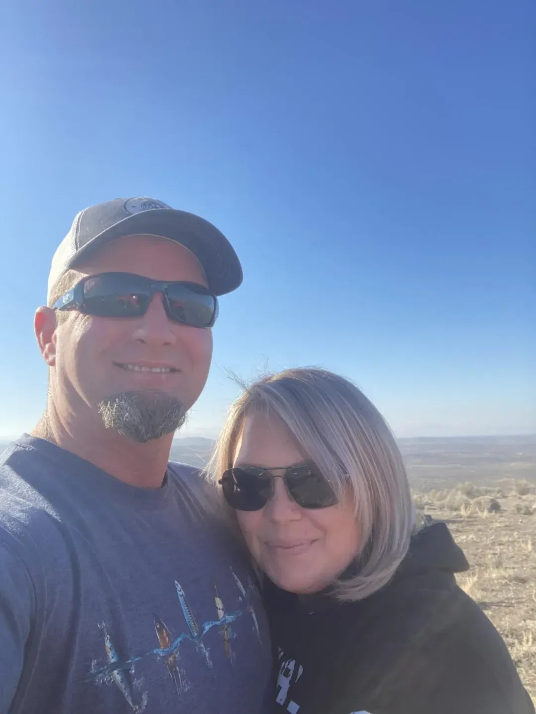 Couple with sunglasses smiles outside under blue sky.