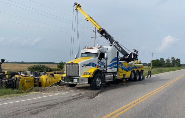 Yellow tow truck lifts a yellow overturned vehicle from the side of a road.