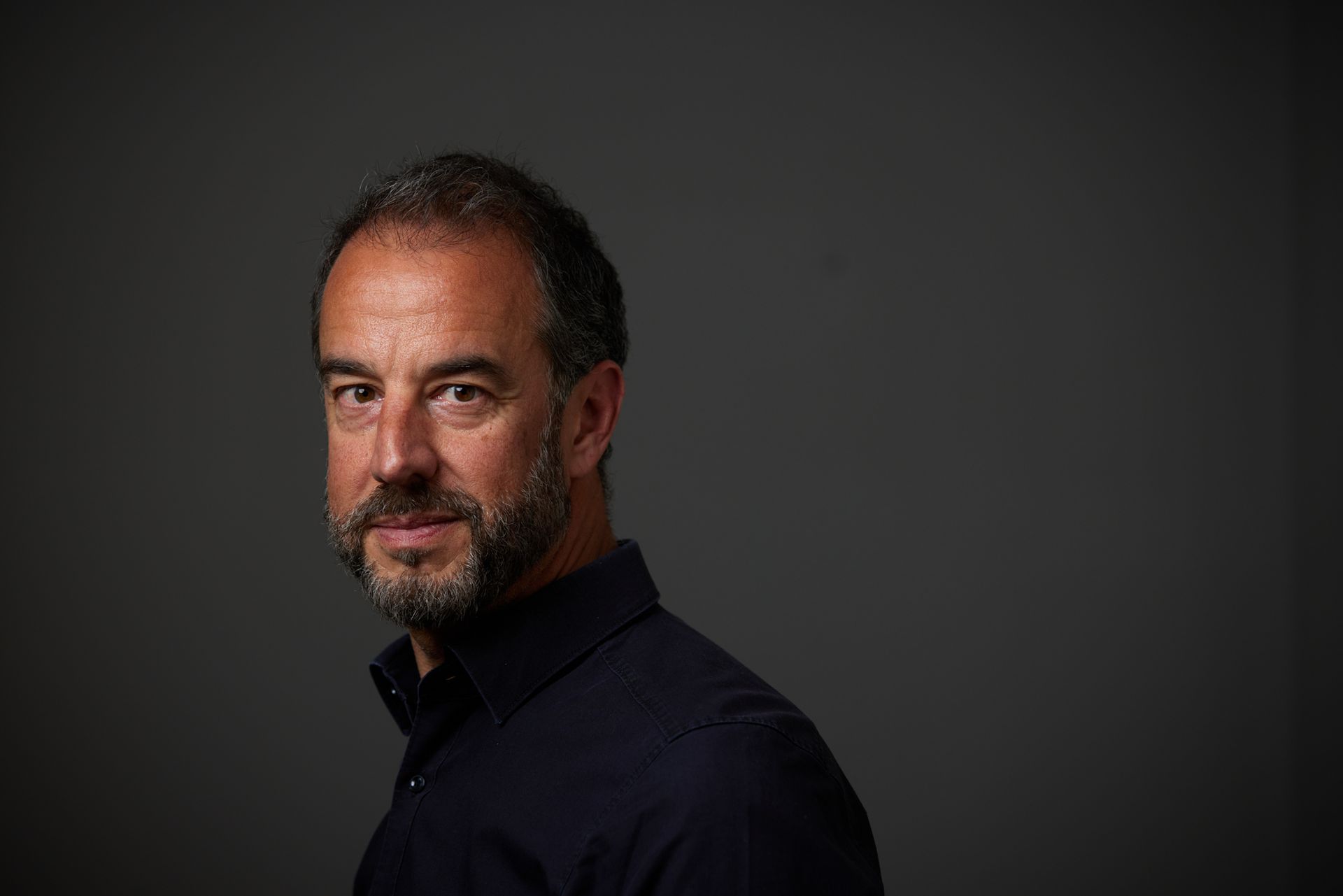 Holger HEID vor einer grauen Wand, er trägt ein schwarzes Hemd