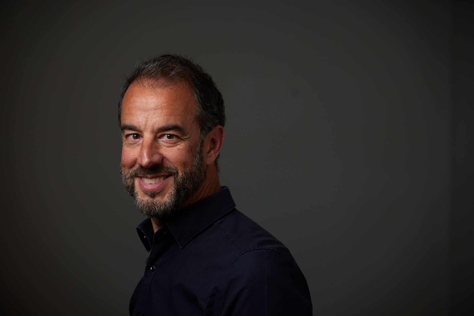 Holger HEID sourit dans la camera devant un fonds gris foncé 