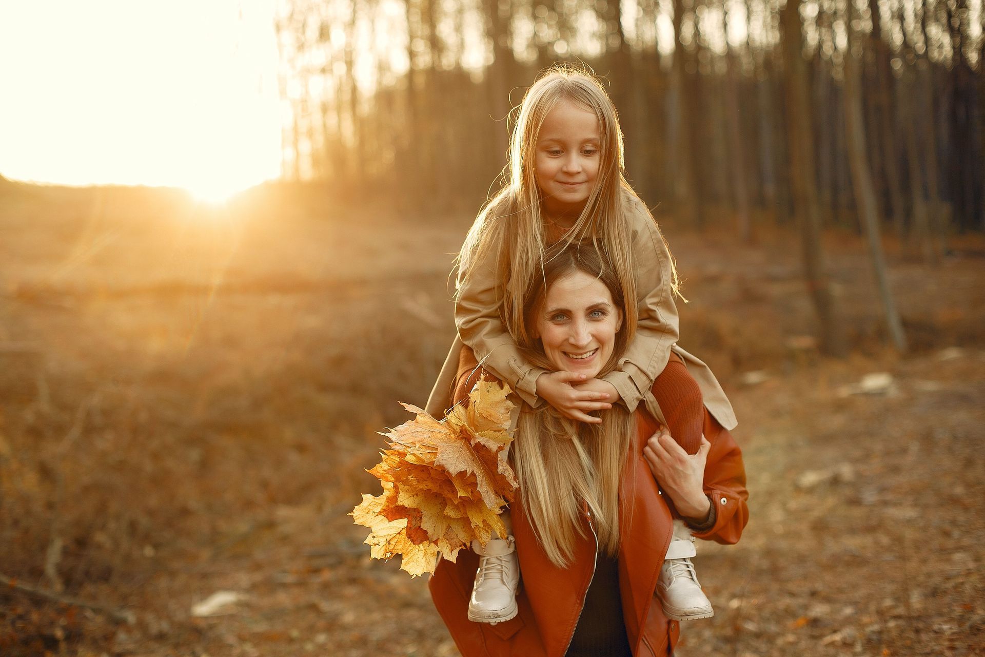 Last oder Freude? Tochter sitzt auf den Schultern ihrer Mama, die lächelt und Laubblätter im Wald gesammelt hat