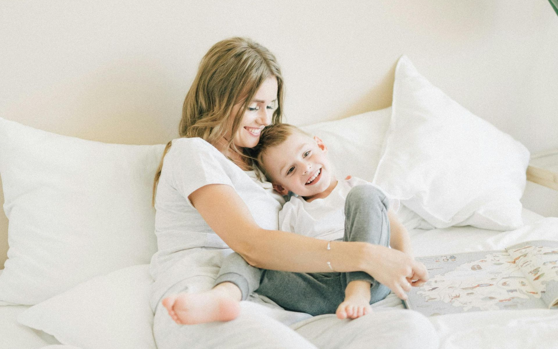 eine junge Mutter liegt mir ihrem ca. 5 jährigen Sohn im Bett. Er liegt in ihren Armen und sie lachen beide.