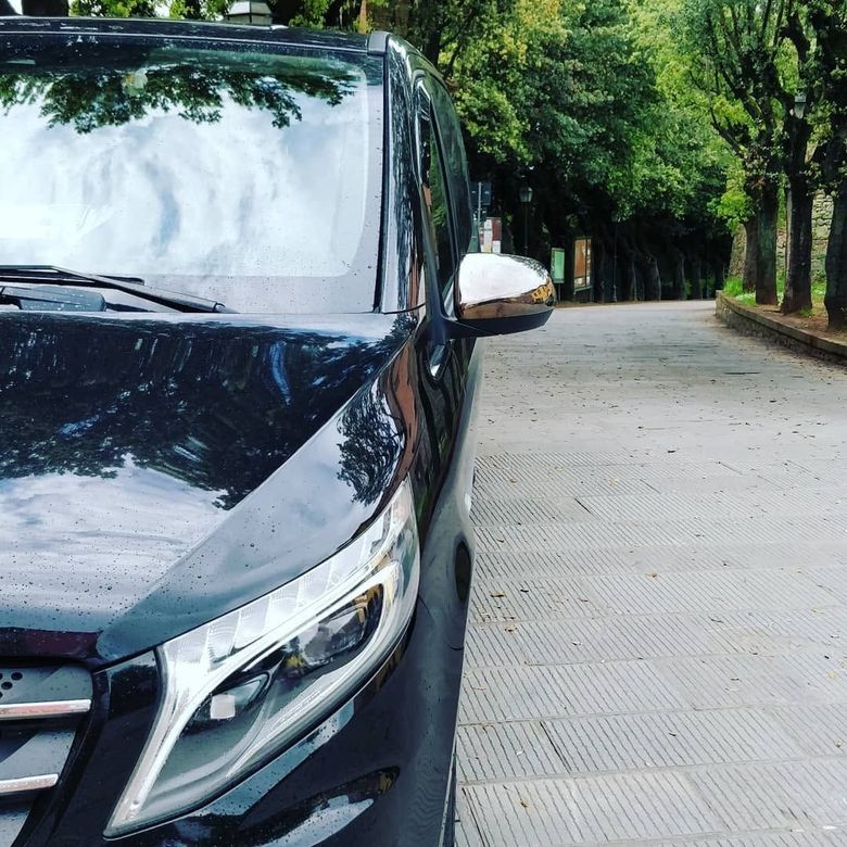 Un'auto nera parcheggiata su una strada alberata, con un veicolo bianco alle sue spalle.