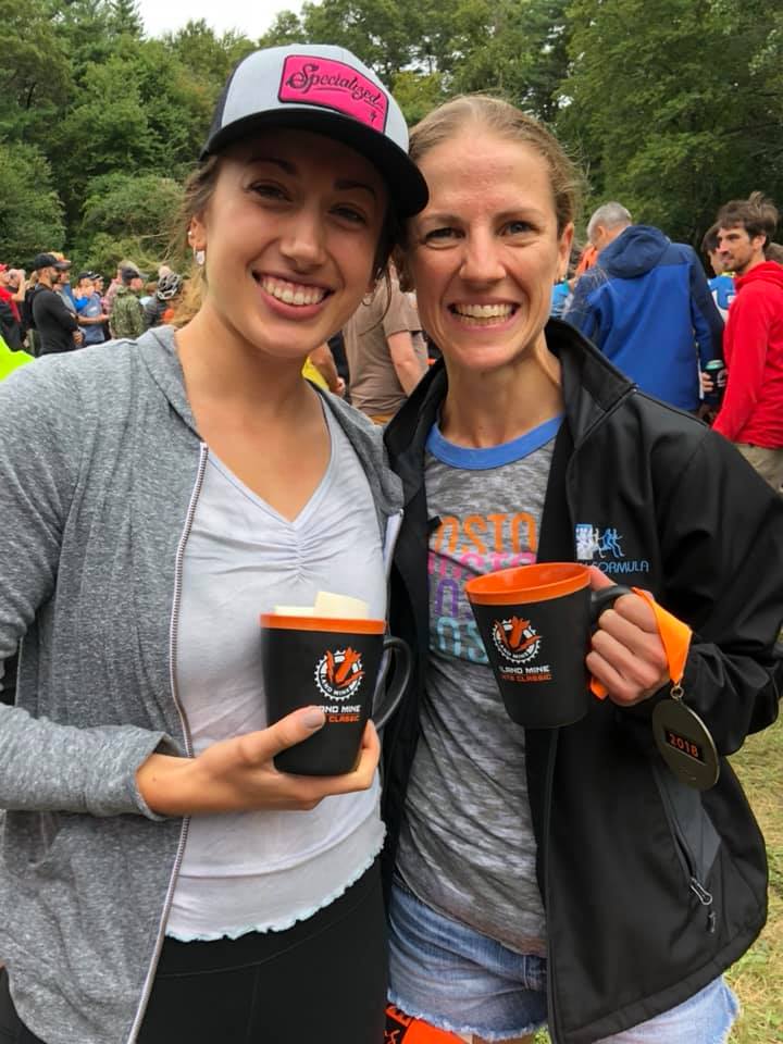 Two smiling people holding orange-lidded cups outdoors at an event