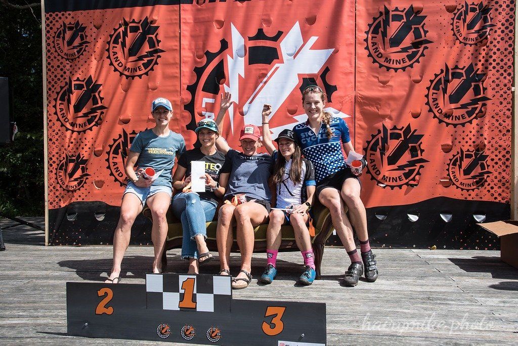 Four rollerskaters pose on a winners podium in front of an orange event banner.