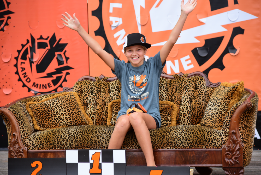 Smiling child on leopard-print couch, arms raised, in front of orange Nickelodeon-themed backdrop