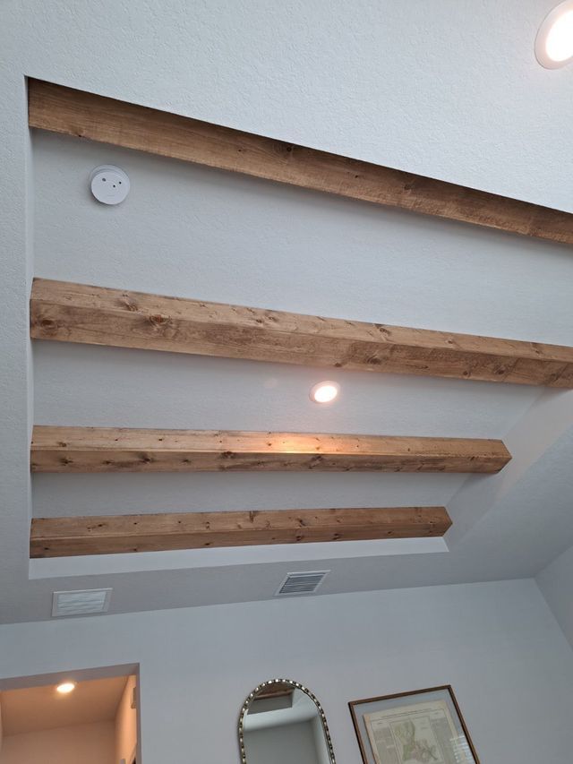 The ceiling of a room with wooden beams and a mirror.
