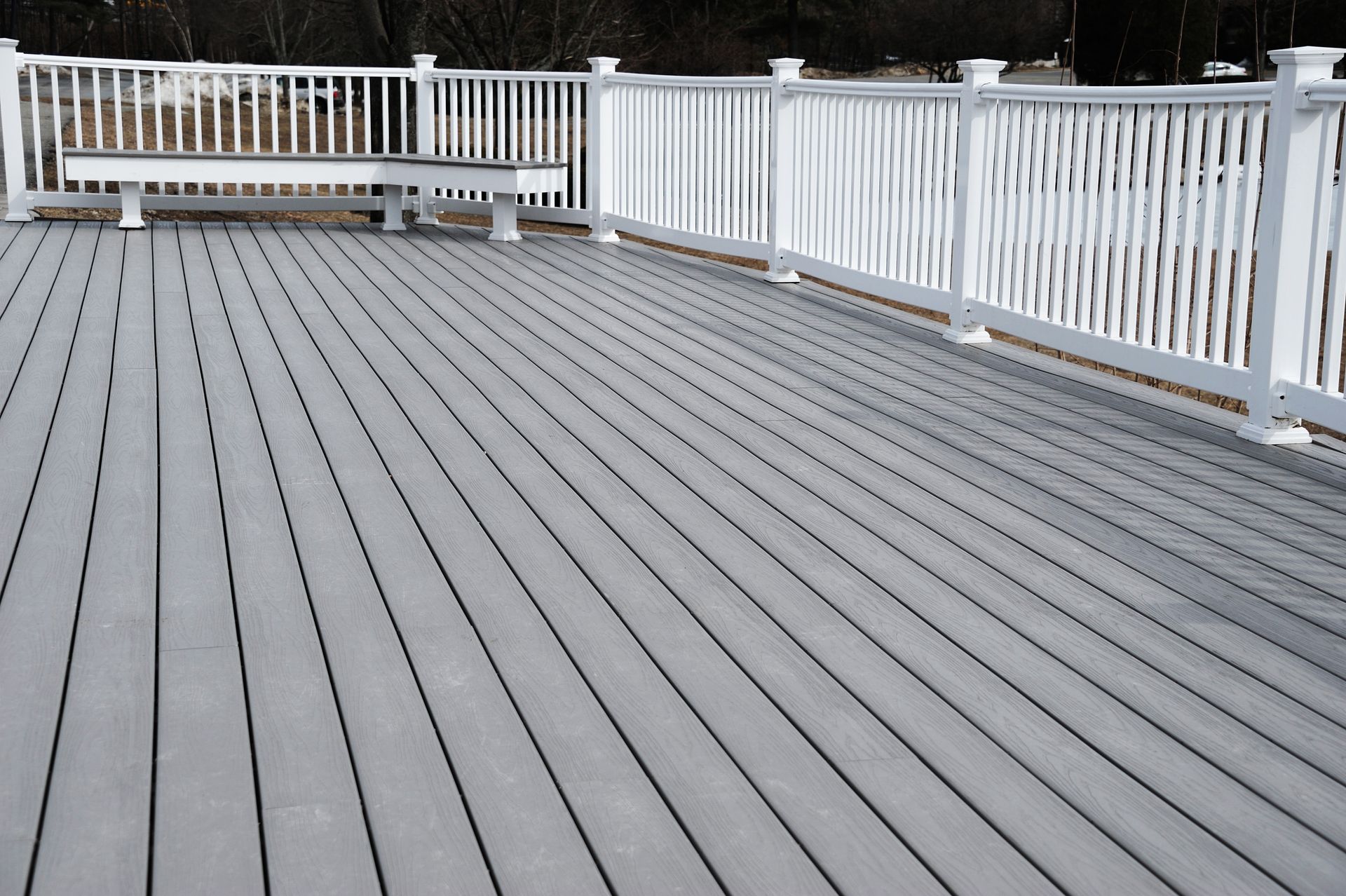 A gray deck with a white railing and a bench